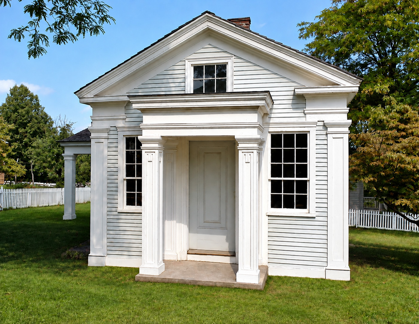 Small greek revival style building with shingle siding featuring a covered porch entrance and window mouldings.