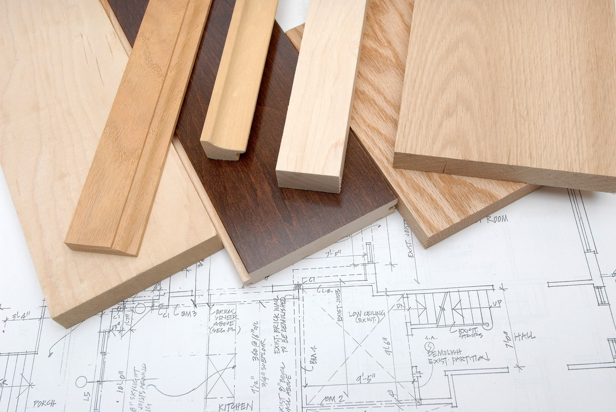 Various wood moulding and millwork samples in different finishes laid out on architectural blueprints