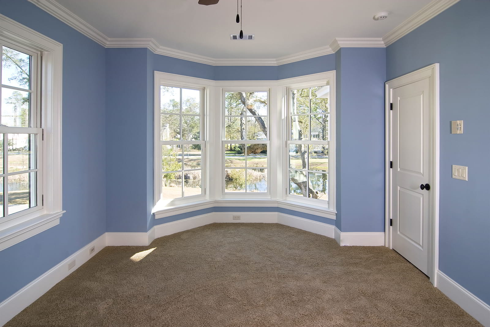 Bay window with white window casing, crown molding, and baseboard trim in a blue room